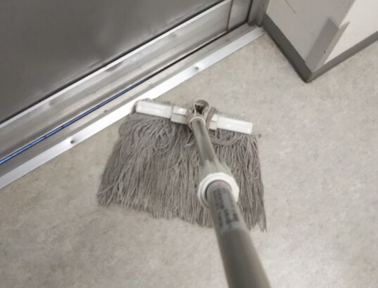 モップで床の壁際を拭く
